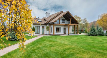Exterior of residential suburban cottage with balcony surrounded with lush green plants and trees