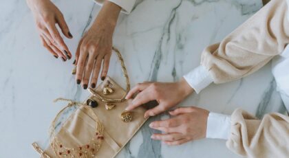 A sophisticated display of gold jewelry and hands on a marble surface, exuding luxury and elegance.