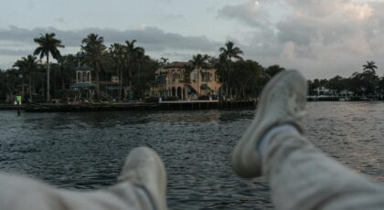 Casual perspective of a tropical waterfront villa with palm trees at sunset.