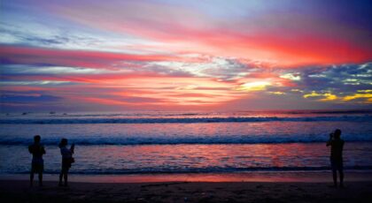 Silhouetted people capturing a stunning sunset over Kuta Beach's vibrant seascape.