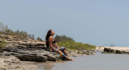 Pregnant woman sitting on a rocky beach, enjoying the scenic view and tranquility.