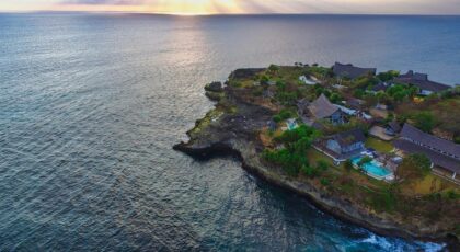 Stunning aerial view of Nusa Penida's coastline at sunset, featuring villas and lush greenery.