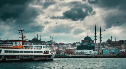 Picturesque scenery of famous New Mosque located on shore of Bosporus with floating ship against cloudy sky in Istanbul