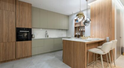 Interior of bright modern kitchen with cupboards near chairs with counter decorated with glasses and plates under lamps next to shelves on wall