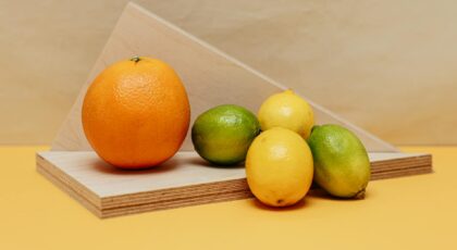 A vivid arrangement of citrus fruits including orange, lemons, and limes on a geometric wooden display against a neutral backdrop.