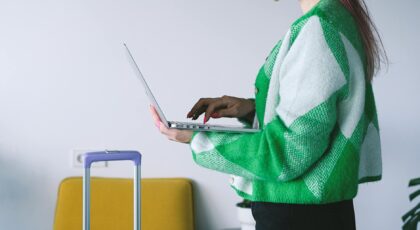 Young woman working on laptop near luggage in stylish hotel lounge, embracing the digital nomad lifestyle.