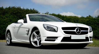 Stunning white Mercedes Benz convertible parked on the road against a lush green backdrop.