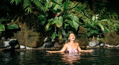 Smiling woman in a tropical jungle pool surrounded by lush greenery.