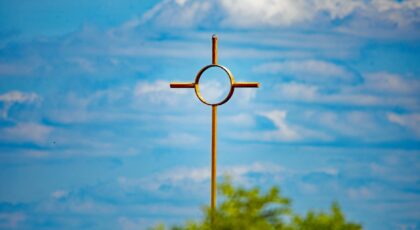 A golden cross stands against a vibrant blue sky and clouds, symbolizing faith and spirituality.