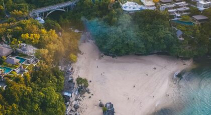 Discover the stunning coastal landscape of Bali with lush greenery and teal waters from above.