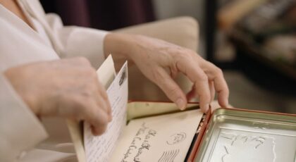 A person is opening a red tin box filled with vintage letters and postcards, capturing nostalgia.