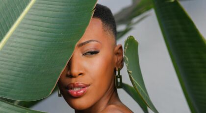 Beautiful portrait of a woman partially hidden behind lush tropical leaves.