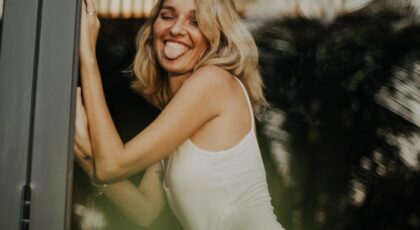 Blonde woman in swimsuit posing playfully by the window in Bali. Outdoors, lively and tropical setting.