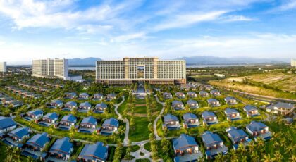 Aerial view of a luxurious tropical resort with modern architecture, palm trees, and blue sky.