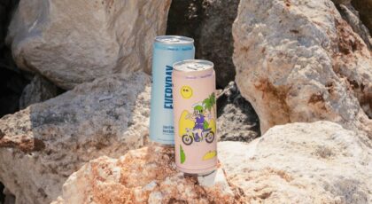 Two drink cans on rocky beach in Bali, showcasing vibrant designs against natural stones.