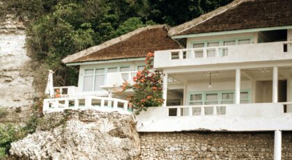 Beautiful villa perched on a cliff overlooking the ocean, surrounded by lush greenery.
