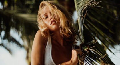 A blonde woman poses with palm leaves in Bali, exuding tropical vibes.