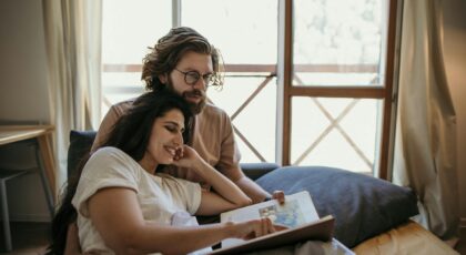 A couple enjoys a cozy morning reading together in their bedroom, embracing love and togetherness.