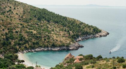 A picturesque coastal cove with a lush hillside and clear blue waters, ideal for travel enthusiasts.