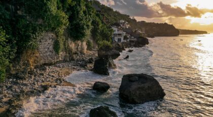 Scenic view of Bali coastline with rock formations and lush greenery at sunrise.