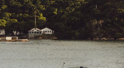 A small boat sails on a tranquil lake with a lush green hill and hilltop chapel in the background.