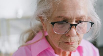 Close-up of an elderly woman with eyeglasses in a thoughtful pose indoors.