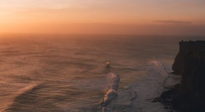 Stunning sunset view over ocean cliffs in Bali, Indonesia with waves crashing ashore.