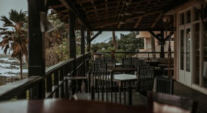 An idyllic seaside patio with empty wooden chairs, surrounded by lush tropical foliage.