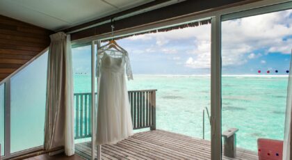 A wedding gown hanging in a Maldives overwater villa with a stunning ocean view, perfect for a beach wedding setting.