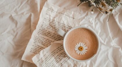 A cup of coffee with a daisy on a bed of book pages and flowers, creating a cozy, artistic scene.