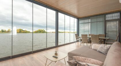 Spacious and modern living room with glass walls offering a serene lake view. Perfect for relaxation.