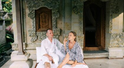 A couple in robes enjoy a relaxing moment outside a Balinese villa with ornate carvings.