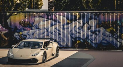 A sleek luxury sports car parked in front of a vibrant graffiti wall under bright daylight.