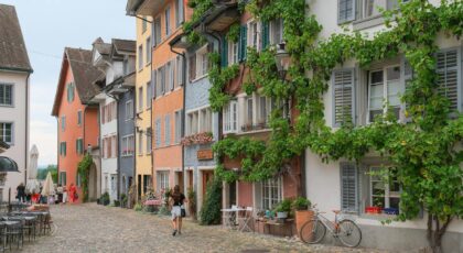 Scenic European street lined with colorful, ivy-draped houses and cobblestone pavement.