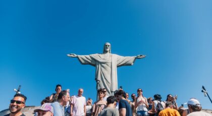 Tourists gather at the iconic Christ the Redeemer statue under clear blue skies in Rio de Janeiro, Brazil.