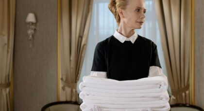 Elegant hotel housekeeper holding fresh, neatly folded white towels in a luxurious room.