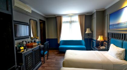 Luxurious hotel room featuring two beds, a blue sofa, artwork, and contemporary furniture.