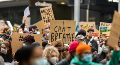 A diverse crowd protesting in Melbourne, holding signs against racism and for justice. Faces covered with masks.