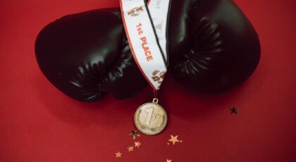 Black boxing gloves with a gold medal on a red background, symbolizing victory and success.