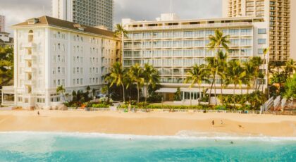 Beachfront hotel surrounded by palm trees and turquoise ocean waves in a tropical travel destination.