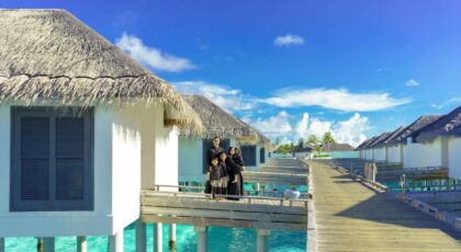 Family enjoys a sunny day on a resort's boardwalk with overwater bungalows and clear blue sky.